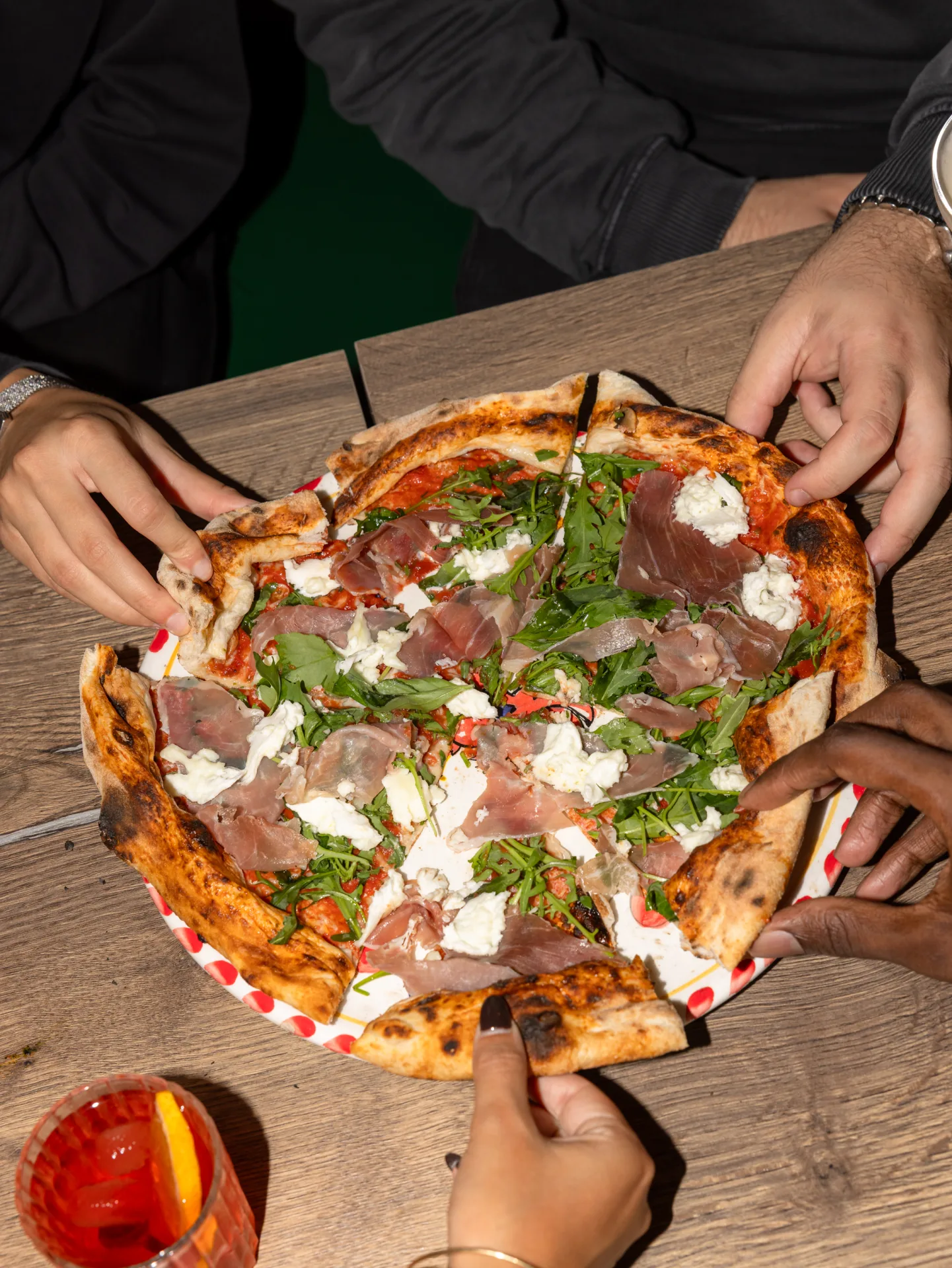 Le mani intorno a una pizza da condividere